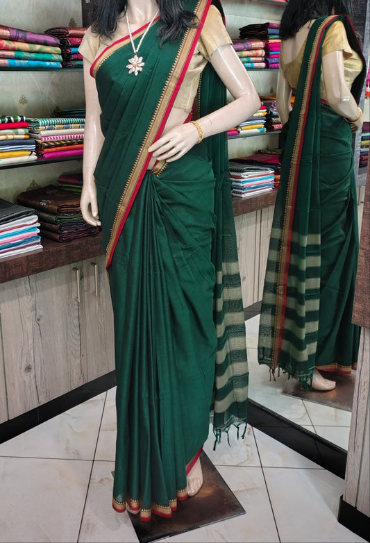A dark green cotton saree with a beige and green striped pallu and border, displayed on a mannequin in a fabric store.